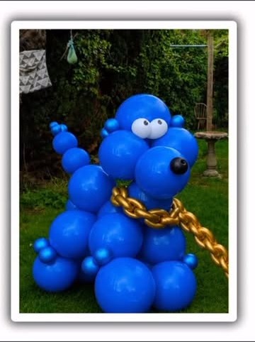 Blue balloon dog sculpture with gold chain, garden setting